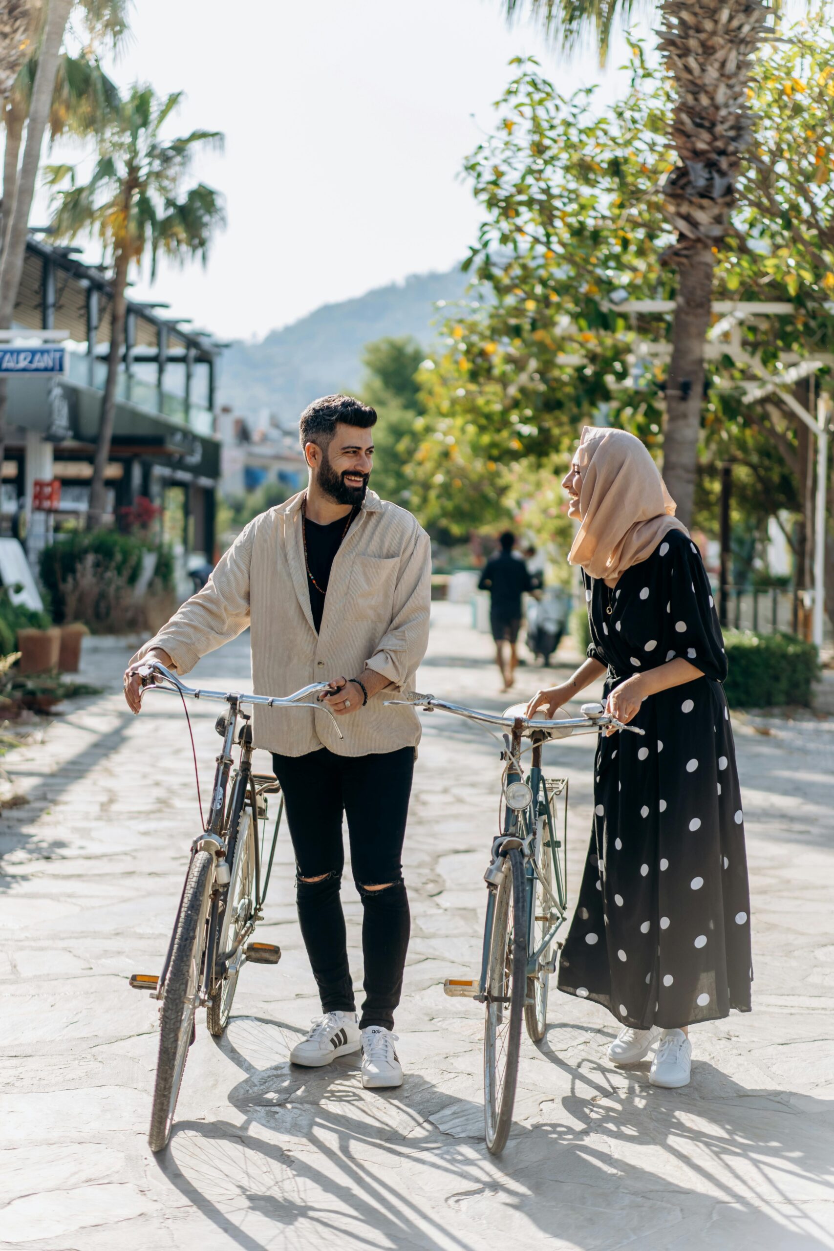 A smiling couple walking with bicycles along a sunny path, enjoying a casual outing.